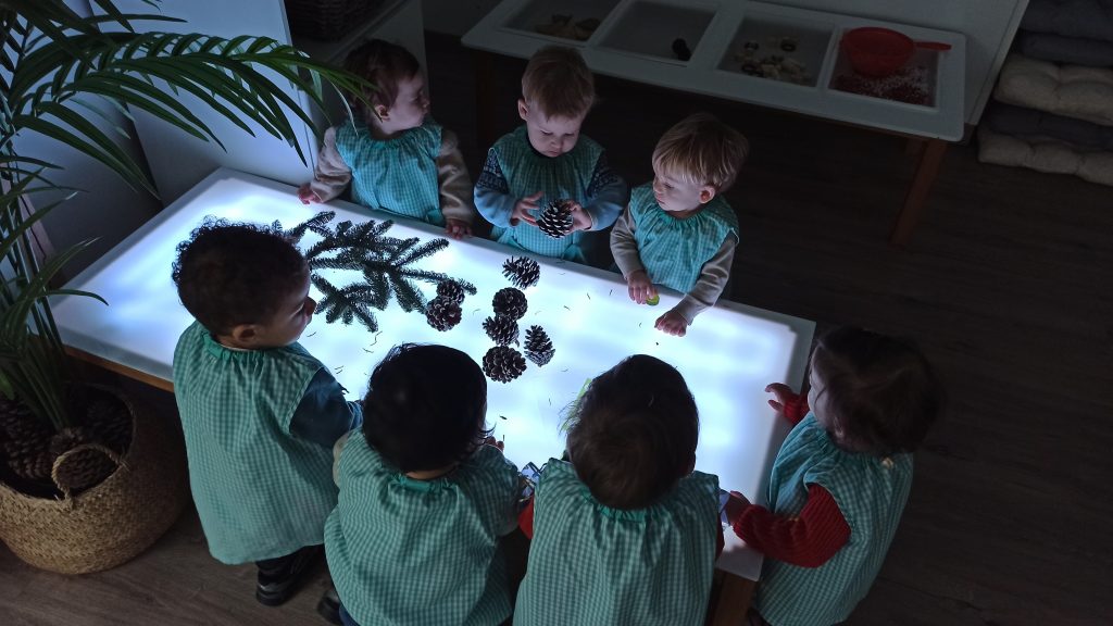 Alumnos de la escuela infantil be you en el atelier naturaleza realizando una actividad en la mesa de luz con elementos naturales como piñas, hojas, o ramas de árbol